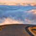 A winding road leading towards clouds and an open horizon far from a need to control